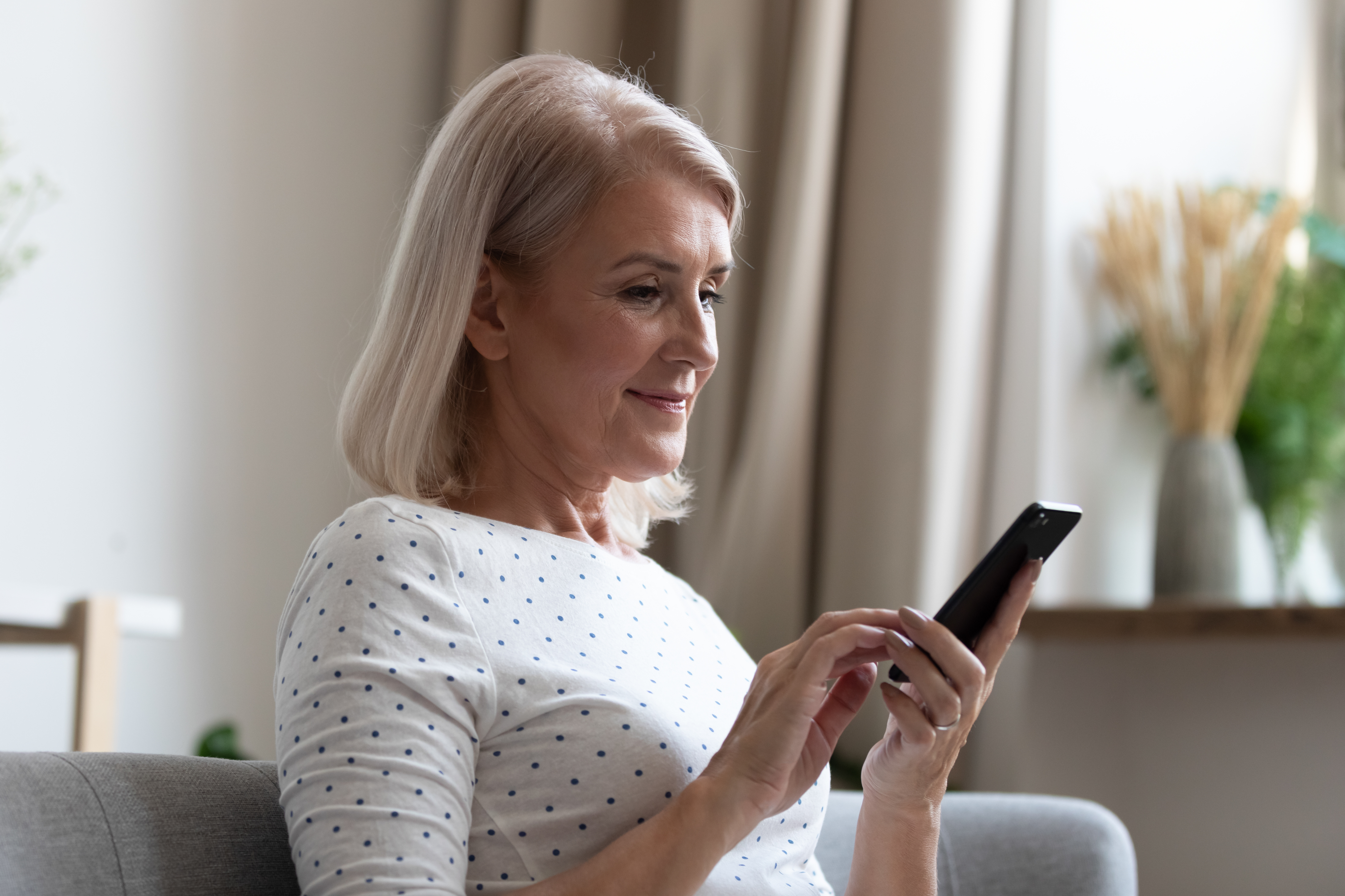 Happy middle aged woman using mobile apps texting at home