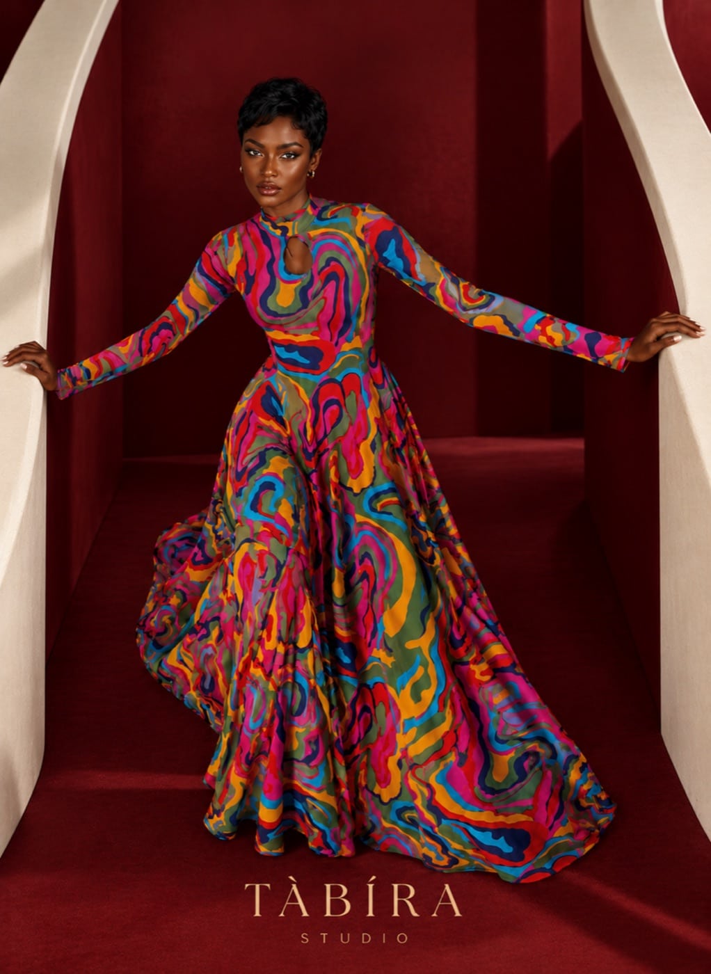 TÀBÍRA Studio model in a flowing multicoloured swirl-print gown on a red staircase